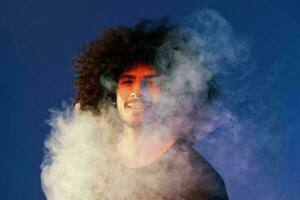 porträtt av en eleganta man med lockigt hår i rök på en blå bakgrund multinationella, Färg ljus, trend foto