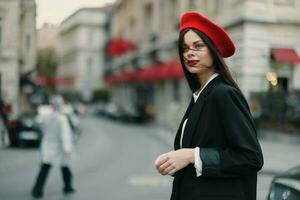 mode kvinna porträtt stående på de gata i främre av de stad i eleganta kläder med röd mun och röd basker, resa, filmiska Färg, retro årgång stil, urban mode livsstil. foto