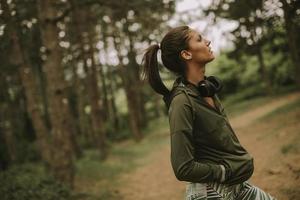ung vacker kvinnlig löpare som lyssnar på musik och tar en paus efter att ha joggat i en skog foto