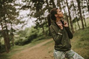 ung vacker kvinnlig löpare som lyssnar på musik och tar en paus efter att ha joggat i en skog foto