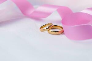 gyllene bröllop ringar för engagemang. äktenskap gyllene ringar med vit, rosa band bakgrund. ringar på de vit och röd reste sig. de äktenskap ringar är de symbol av traditionell bröllop av par älskare. foto