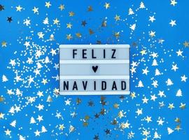 ljusruta med feliz navidad fras, spansk god jul på en blå bakgrund med konfetti. foto