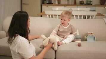 Lycklig familj på Hem. mor och bebis pojke spelar med leksaker i soffa på Hem inomhus. liten litet barn barn och barnvakt barnskötare har roligt tillsammans. ung kvinna mamma unge son resten i levande rum. foto