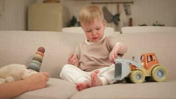 Lycklig familj på Hem. mor och bebis pojke spelar med leksaker i soffa på Hem inomhus. liten litet barn barn och barnvakt barnskötare har roligt tillsammans. ung kvinna mamma unge son resten i levande rum. foto