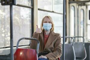 kvinna med skyddande ansikte mask i buss transport. ung kvinna bär skyddande ansikte mask, hon Sammanträde i buss transport i de stad.. kvinna med mask i buss foto