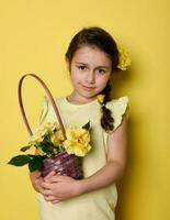 caucasian liten flicka i gul elegant ha på sig och blommor i hår, innehav bukett av ro i korg, leende på kamera foto