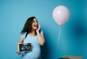 gravid kvinna upplever glädje tittar på en rosa ballong flygande ut av en låda, innehav ultraljud skanna av henne framtida barn foto