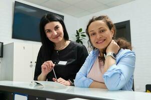 kvinna tandläkare och gravid patient leende ser på kamera, stående på reception disken i modern dental klinik foto