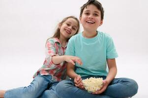 preteen pojke och liten flicka, bror och syster tittar på tecknade serier äter popcorn. ungar. livsstil. underhållning foto