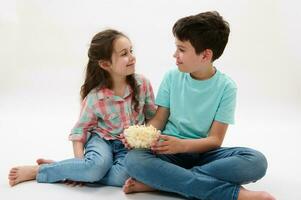 Lycklig preteen pojke och flicka äter popcorn, leende talande till varje Övrig, isolerat vit bakgrund. barndom. familj foto