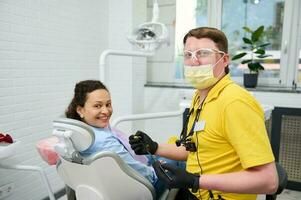 behörig manlig tandläkare läkare och Lycklig kvinna patient, leende ser på kamera. gravid kvinna på dental utnämning foto