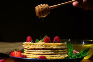 hand innehav trä- pinne med droppande honung på nyligen bakad pannkakor för skrava tisdag, isolerat på svart bakgrund foto