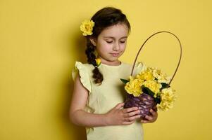 söt liten flicka med reste sig blommor i frisyr, innehav korg- korg full av gul rosor, isolerat studio bakgrund. foto