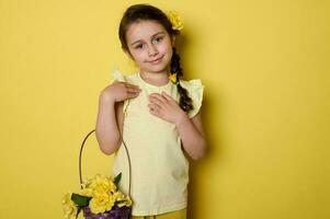 emotionell porträtt av förtjusande liten barn flicka bär gul klänning, innehav lila korg- korg med gul ro foto