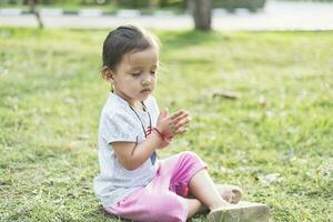 liten asiatisk flicka praktiserande mindfulness meditation utomhus- i en parkera. foto