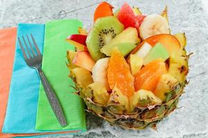 färsk fruktsallad med kiwi, banan, persika, apelsin, röd apelsin, aprikos och melon i handgjord ananasskål. foto