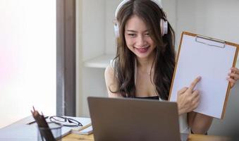 stående av den attraktiva asiatiska kvinnan som ser kameran som ler med förtroende som arbetar med den smarta minnestavlan och positivt livsstilskoncept på kaféet foto