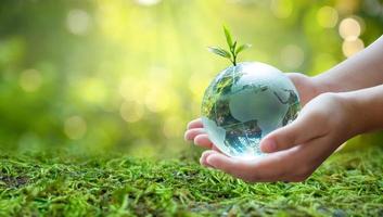 en man med ett glasjordklot koncept dag jorden rädda världen spara miljö världen är i gräset av den gröna bokehbakgrunden