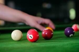 mannens hand och kö ärm spelar snooker spel eller framställning siktar till skjuta slå samman bollar på en grön biljard tabell. färgrik snooker bollar på grön fris. foto