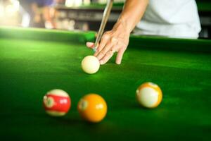 mannens hand och kö ärm spelar snooker spel eller framställning siktar till skjuta slå samman bollar på en grön biljard tabell. färgrik snooker bollar på grön fris. foto