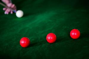 mannens hand och kö ärm spelar snooker spel eller framställning siktar till skjuta slå samman bollar på en grön biljard tabell. färgrik snooker bollar på grön fris. foto