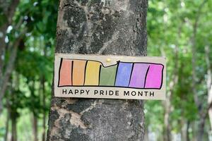 vägvisare som har regnbåge teckning med texter 'Lycklig stolthet månad' fastnat på träd trunk i offentlig parkera till fira och till hälsa HBTQ människor evenemang i stolthet månad och till respekt kön mångfald. foto