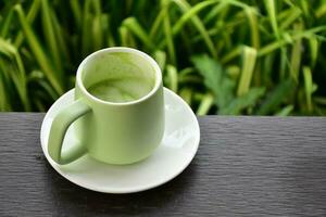 en kopp av grön te på trä- tabell bredvid blomma säng. foto