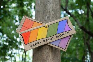 vägvisare som har regnbåge teckning med texter 'Lycklig stolthet månad' fastnat på träd trunk i offentlig parkera till fira och till hälsa HBTQ människor evenemang i stolthet månad och till respekt kön mångfald. foto