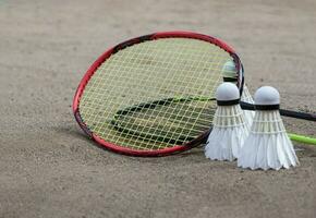 badminton utrustning, racketar och vit grädde fjäderbollar, på sand golv av utomhus- badminton domstol, selektiv fokus, begrepp för utomhus- aktivitet och utomhus- sporter för hälsa. foto