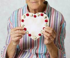 gammal kvinna håller en hjärta i henne händer foto