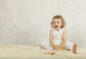 små flicka i en vit klänning är spelar med henne leksaker. foto
