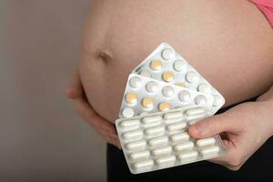 ung gravid kvinna håller filmer av piller stänga till henne mage. foto