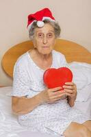 gammal kvinna klädd i santa hatt med röd hjärta i henne händer foto
