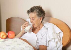 gammal kvinna drycker några mjölk i de morgon- foto