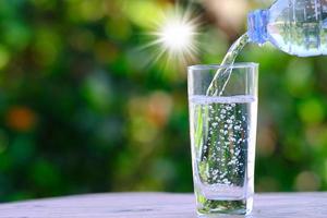 hälla renat färskt dricksvatten från flaskan på träbord och mineralvatten koncept foto