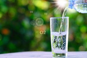 vatten från bouttle som häller i glas på träbord och mineralvattenhälsovårdskoncept, utrymme för text foto