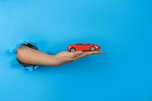 kvinna hand genom blå papper innehav bil modell foto