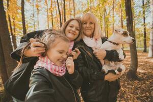 tre generationer av kvinnor och hund känna roligt se på kamera Framställ för självporträtt bild tillsammans, rolig upphetsad barn, mamma och mormor ha roligt njut av helgen ta selfie på grej i höst foto