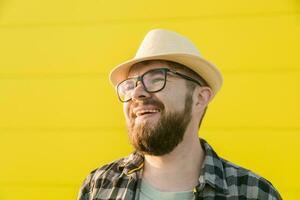 stilig kille turist skrattande Lycklig bär sugrör hatt för reser, stående mot gul vägg bakgrund utomhus foto