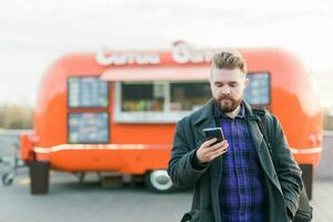 porträtt av stilig ung man med smartphone stående i främre av mat lastbil foto