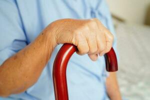 asiatisk äldre handikapp kvinna patient innehav gående pinne i rynkig hand på sjukhus. foto
