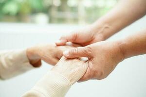 vårdgivare håller händerna asiatisk äldre kvinna patient, hjälp och vård på sjukhus. foto