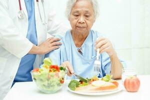 asiatisk äldre kvinna patient äter lax insats och vegetabiliska sallad för friska mat i sjukhus. foto