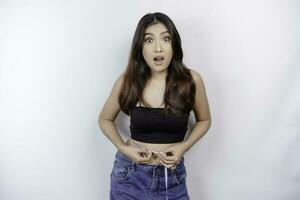 diet livsstil begrepp. chockade asiatisk flicka mätning henne midja med mätning tejp, isolerat förbi vit bakgrund foto