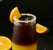 iced kaffe med orange juice i en transparent glas, uppfriskande stappla kaffe på de tabell, svart bakgrund foto