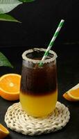iced kaffe med orange juice i en transparent glas, uppfriskande stappla kaffe på de tabell, svart bakgrund foto