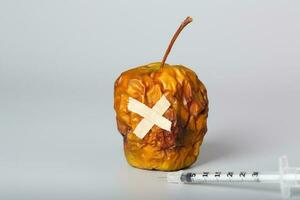 skrumpen äpple och insulin ultra tunn spruta på en grå yta. foto