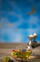 te i en glas kopp med arabicum sötsaker på en trä- yta. foto