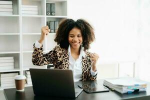 afrikansk företag kvinna är förtjust och Lycklig med de arbete de do på deras läsplatta, bärbar dator och tar anteckningar på de kontor. foto