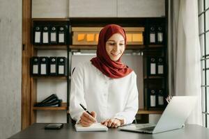 ung arabicum kvinna entreprenör bär en hijab arbetssätt uppkopplad med en bärbar dator på kontor foto